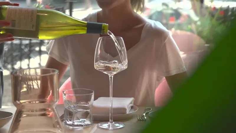 Vino bianco versato in un calice, a un tavolo all'aperto.